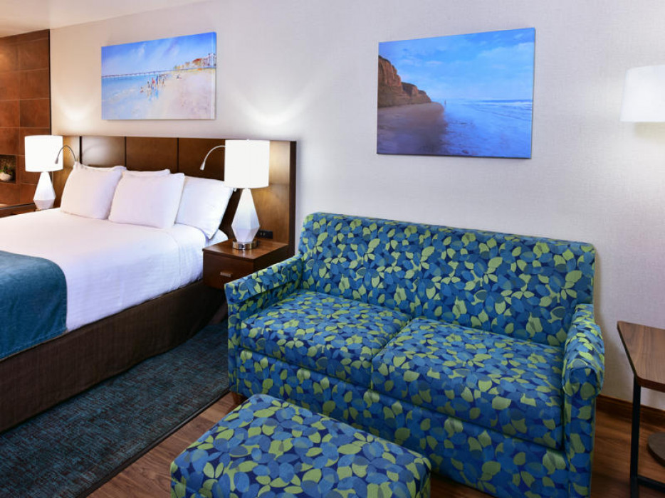 A hotel room with a bed, sofa, and artwork