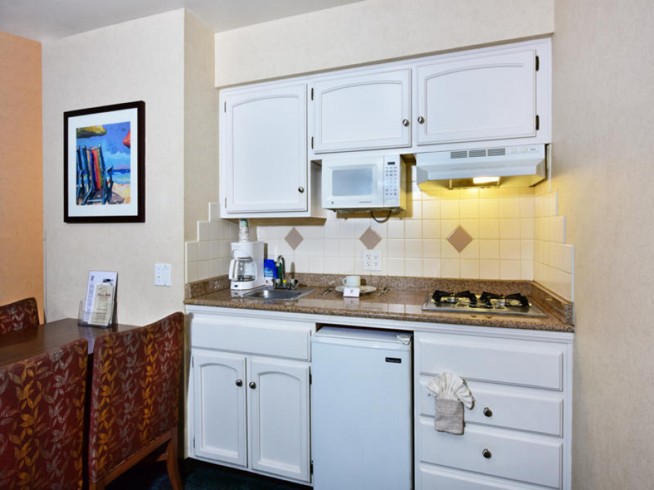 A small kitchenette with white cabinets and brown countertops