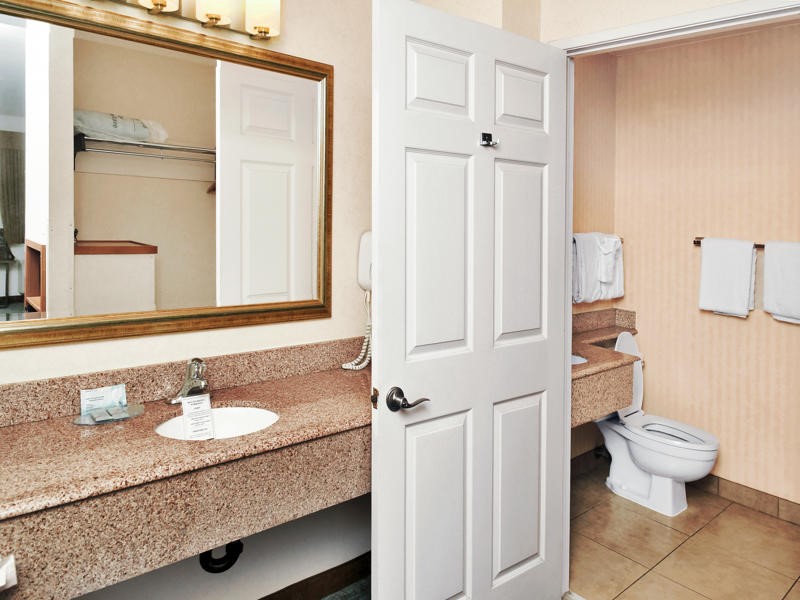A bathroom with a granite countertop, peach walls, and a tiled floor, featuring a sink, toilet, and mirror.