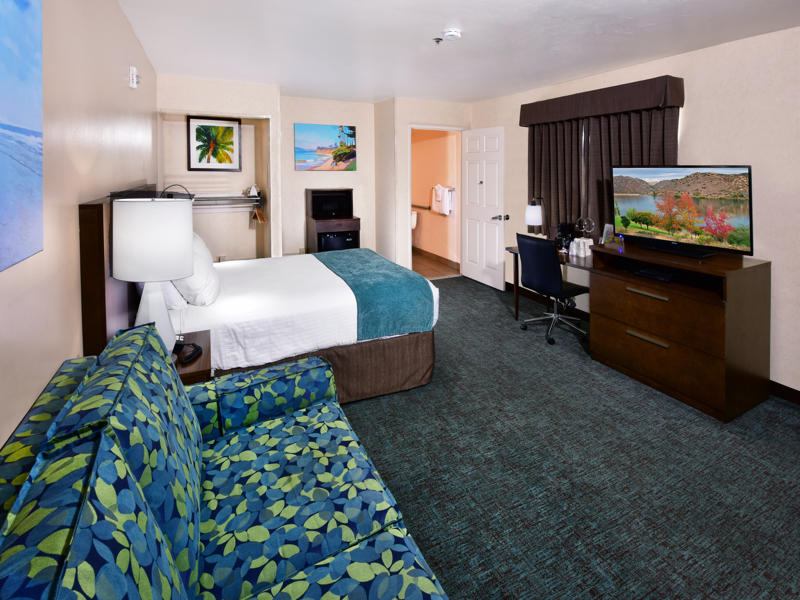 A wide view of a hotel room with a bed, sofa, desk, and TV