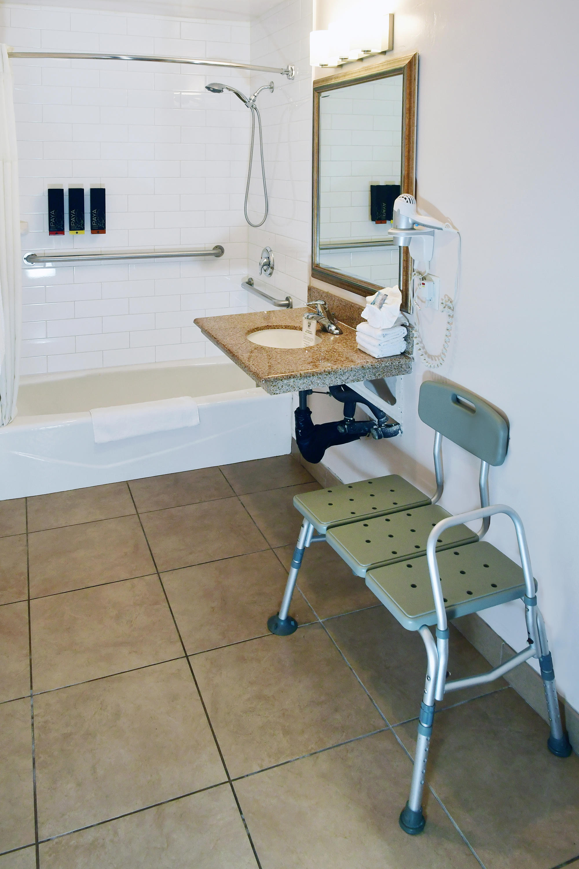 A bathroom with a walk-in shower, grab bars, and a shower chair.