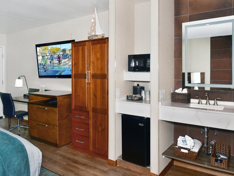A wide view of a hotel room with a desk, TV, microwave, mini fridge, and bathroom sink.