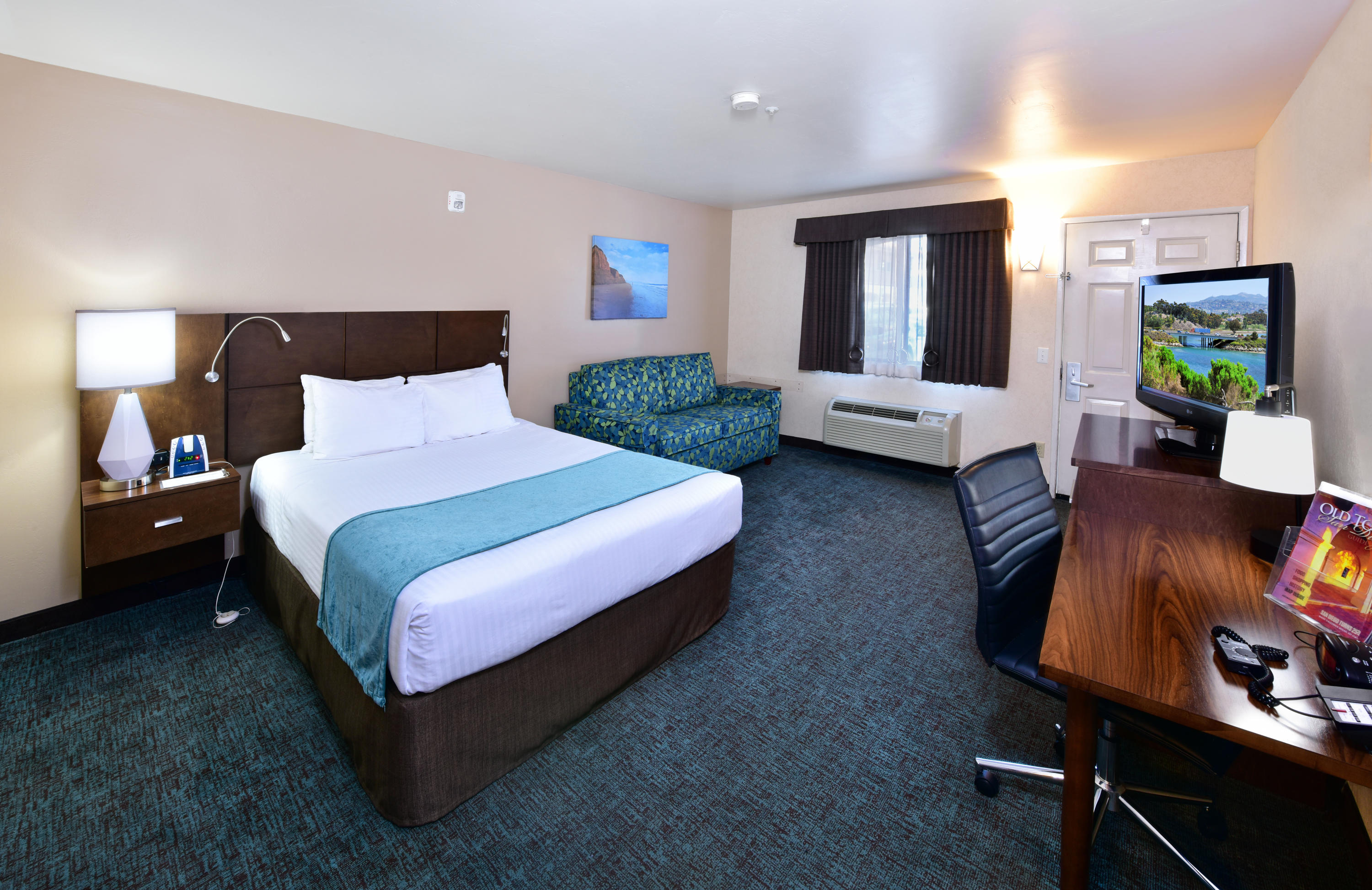 A wide view of a hotel room with a king-sized bed, sofa, desk, and TV.