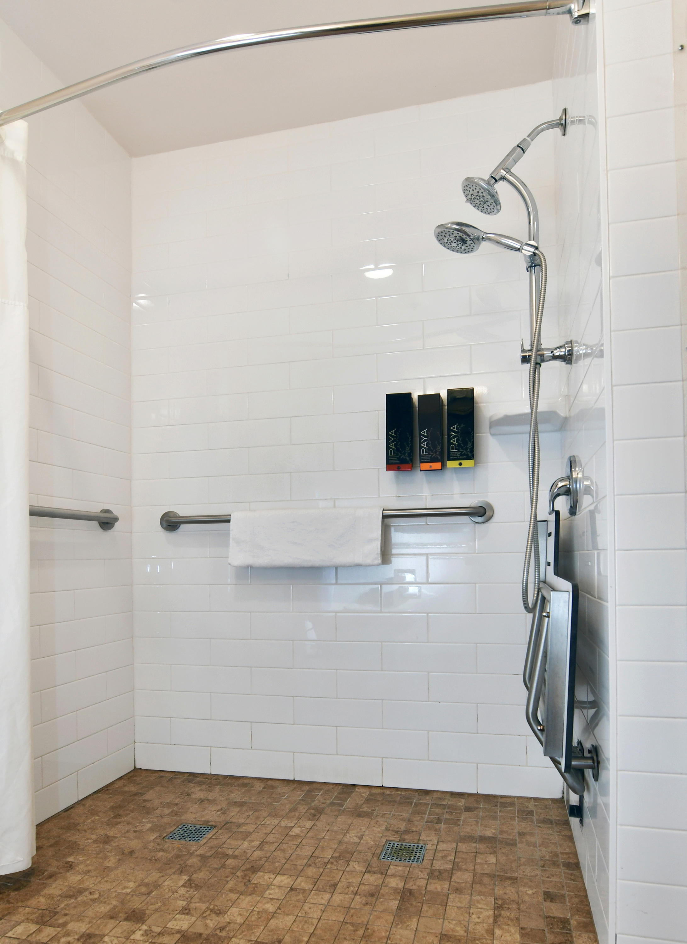 A large walk-in shower with a seat, grab bars, and a rainfall showerhead.