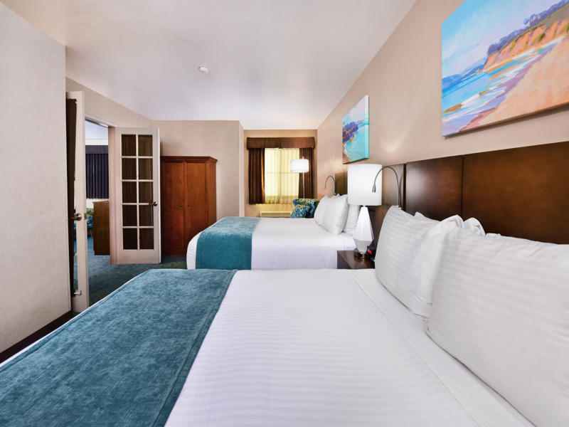A hotel room with two beds, a wardrobe, and a doorway leading to another room.