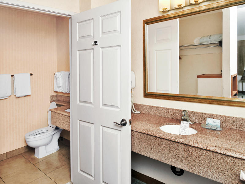 A bathroom with a granite countertop, large mirror, single sink, toilet, and tiled floor.